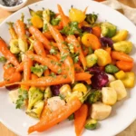 A plate of roasted diced carrots and mixed vegetables, including Brussels sprouts, beets, and squash, garnished with fresh herbs, perfect for a nutritious dinner.